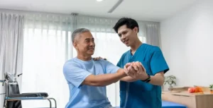Gambar seorang fisioterapis sedang memberikan terapi kepada seorang kakek untuk membantu pemulihan kondisi fisik.