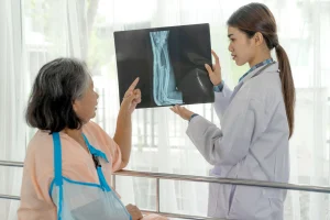 Seorang dokter profesional di ruang konsultasi modern sedang menjelaskan hasil pemeriksaan kepada pasien yang mengalami patah tulang lengan