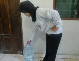 Sebuah gambar mba Ajeng Nandini sedang mengangkat galon